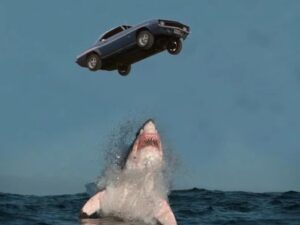 an image of a car suspended in mid-air while a shark emerges from the water trying to swallow it | Agents of Fandom