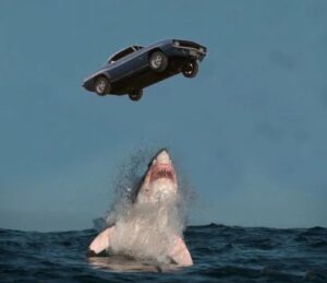 an image of a car suspended in mid-air while a shark emerges from the water trying to swallow it | Agents of Fandom