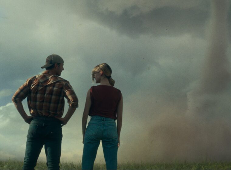 Glen Powell and Daisy Edgar Jones standing with a tonado in the distance in Twisters | Agents of Fandom