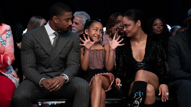 (Left to right): Adonis Creed (Michael B. Jordan), Amara Creed (Mila Davis-Kent), and Bianca Taylor (Tessa Thompson) sitting ringside at a boxing match in Creed III. Image Credit: MGM Studios | Agents of Fandom