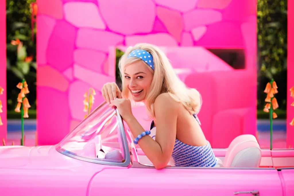 Margot Robbie as Barbie sitting in a pink car, wearing blue attire | Agents of Fandom | Movies of summer 2023