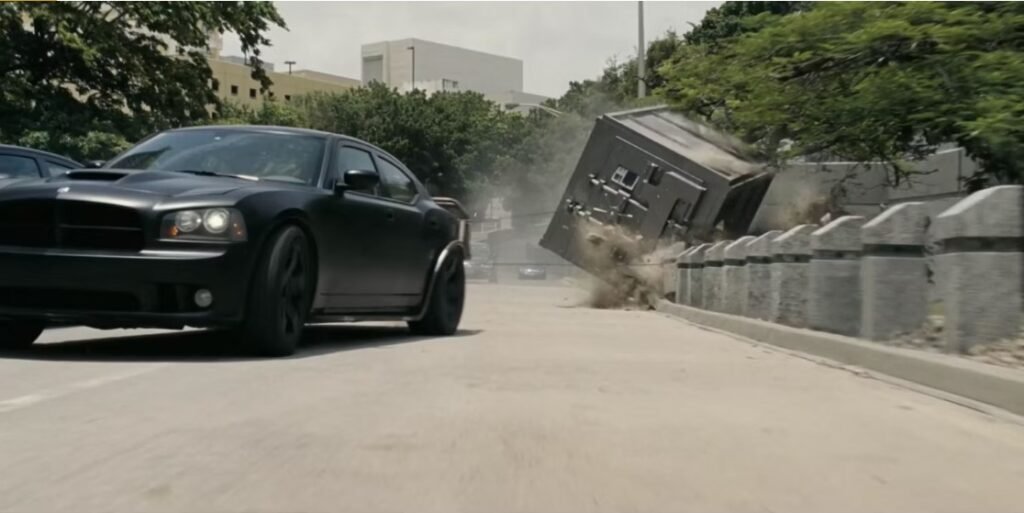 A black Dodge Charger driving with an industrial sized vault attached to the back of it, as seen in Fast Five | Agents of Fandom