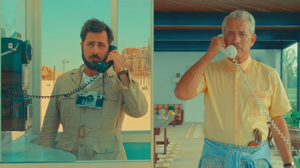 Jason Schwartzman as Augie Steenbeck and Tom Hanks as Stanley Zak holding a phone calling each other in a scene in Asteroid City | Asteroid City Review | Agents of Fandom
