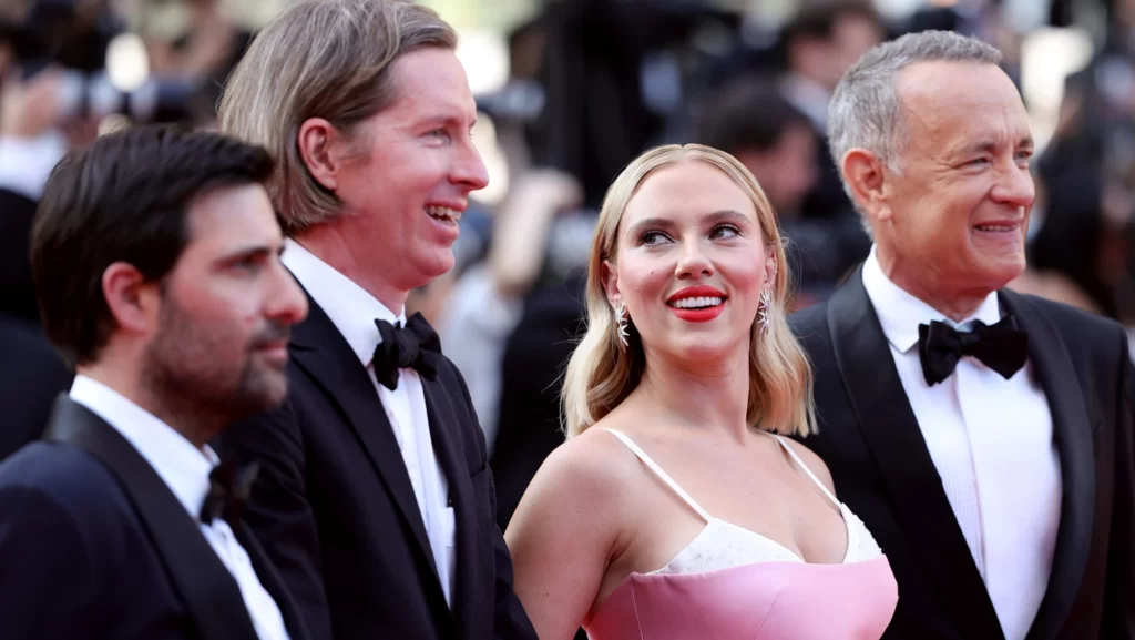 Jason Schwartzman, Wes Anderson, and Tom Hanks looking at the cameras in front of them while Scarlett Johansson looks and admires Wes Anderson | Asteroid City Review | Agents of Fandom
