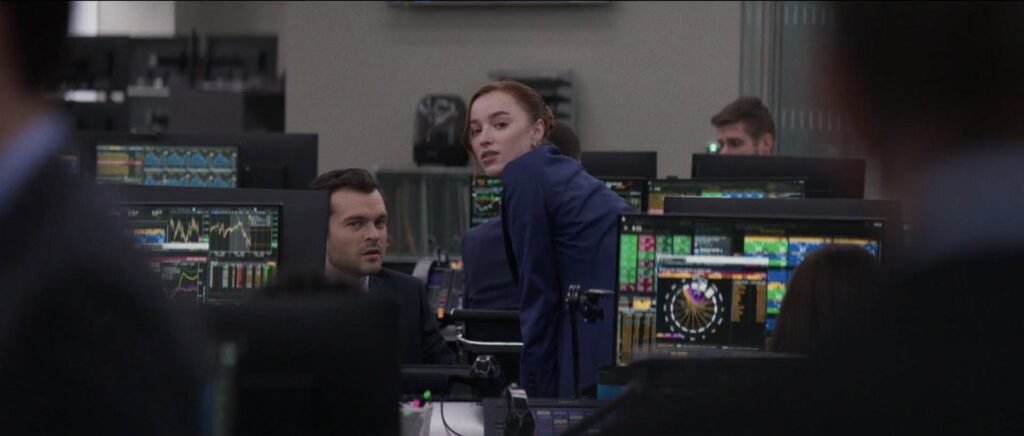 Phoebe Dynevor and Alden Ehrenreich are dressed in suits and are surrounded by computers displaying data and graphs in Fair Play | TIFF 2023 | Agents of Fandom
