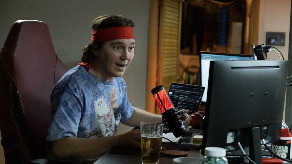 Paul Dano were a red headband look at his computer monitors in a scene in Dumb Money | TIFF 2023 | Agents of Fandom