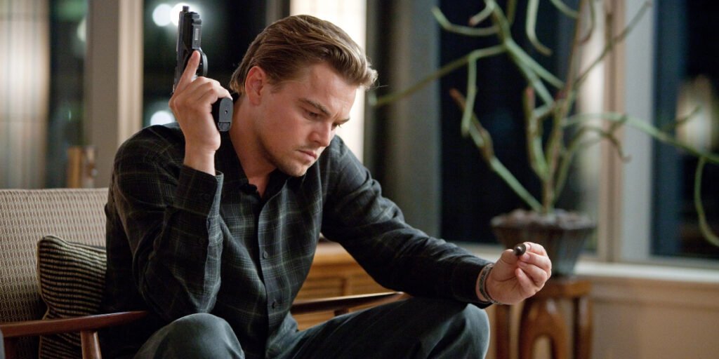 Leonardo DiCaprio sitting in a chair holding a gun and bullet in Inception | Christopher Nolan movies | Agents of Fandom