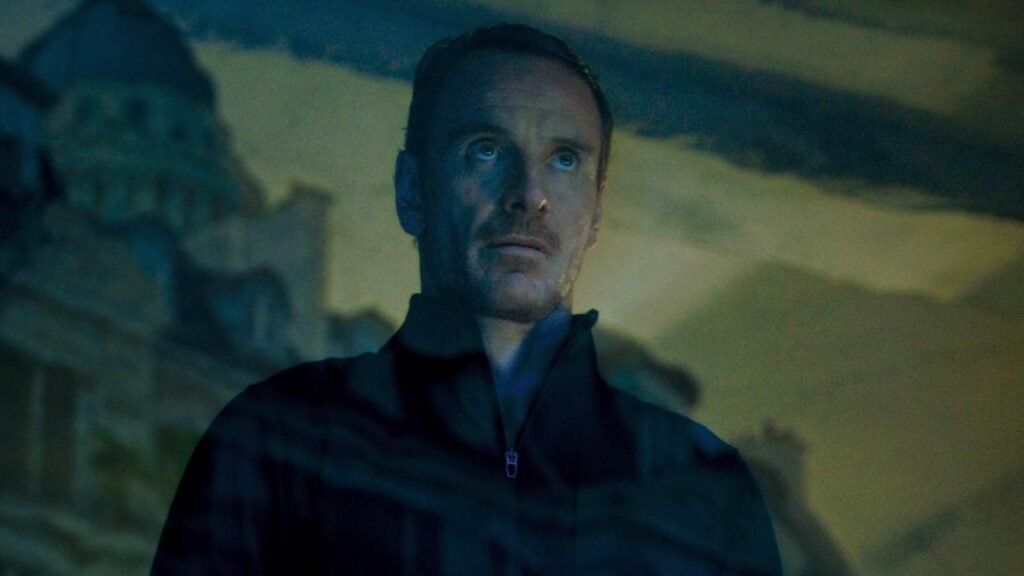 Michael Fassbender as The Killer looking out a window in The Killer | Agents of Fandom