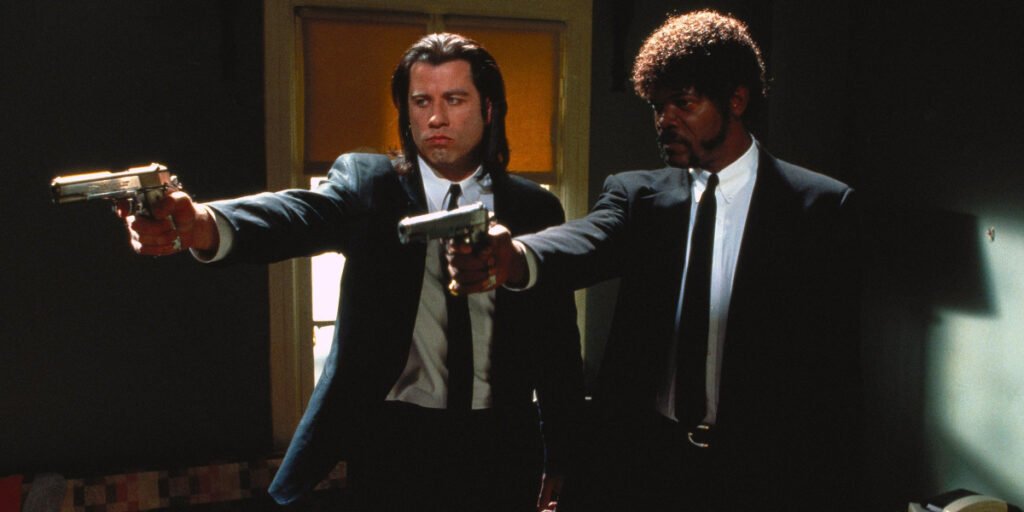 John Travolta as Vincent Vega and Samuel L. Jackson as Jules Winnfield holding pistols in Pulp Fiction | best 90s movies  | Agents of Fandom