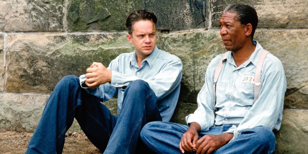 Tim Robbins as Andy Dufresne and Morgan Freeman as Ellis Boyd 'Red' Redding chatting while sitting on the ground leaning on a wall | best '90s movies | Agents of Fandom