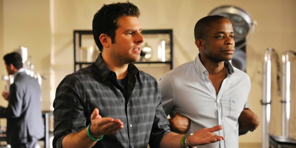 James Roday Rodriguez holding his arms out and Dulé Hill holding his hands beneath his arms in Psych | Agents of Fandom