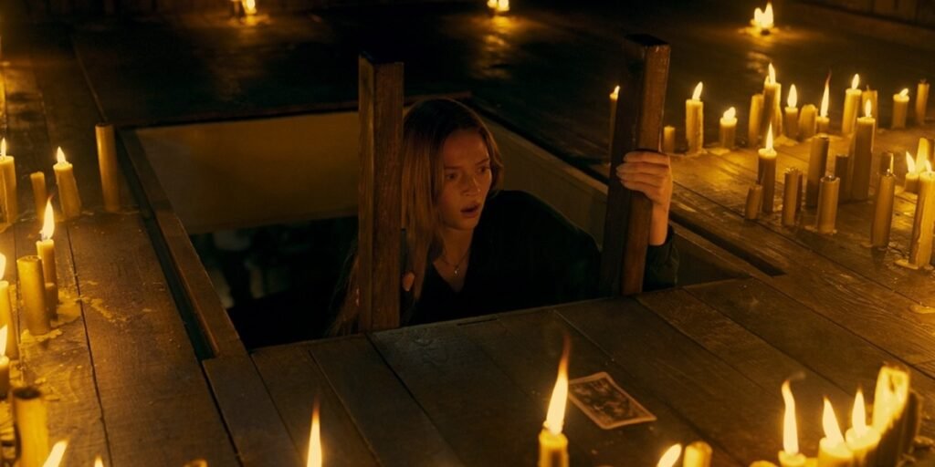Larsen Thompson peeking up out of a hole in the floor into an attic in Tarot 2024 | Agents of Fandom