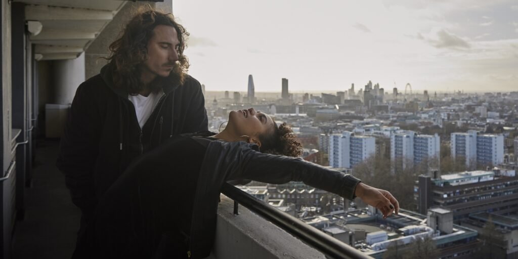 Daniel (Billy Postlethwaite, left) leans over Lena (Emma McDonald) as she leans over a high-rise balcony overlooking London in 7 Keys. I Agents of Fandom