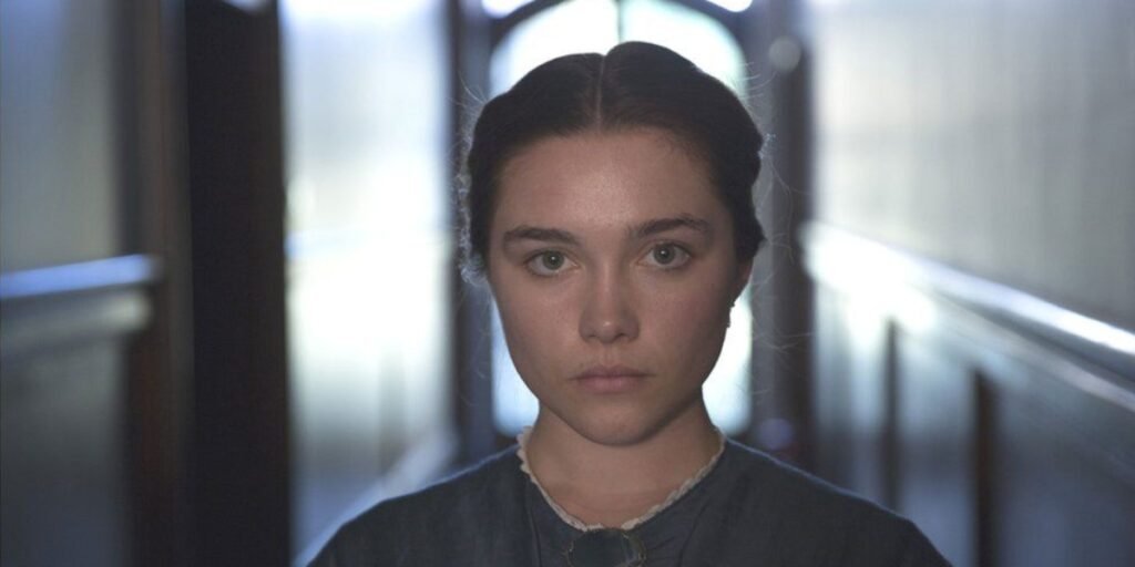 The picture shows young woman (Florence Pugh) with a somber expression. She has dark hair and appears to be sitting or standing in a dimly lit interior space, with blurred lights or windows in the background | Agents of Fandom 