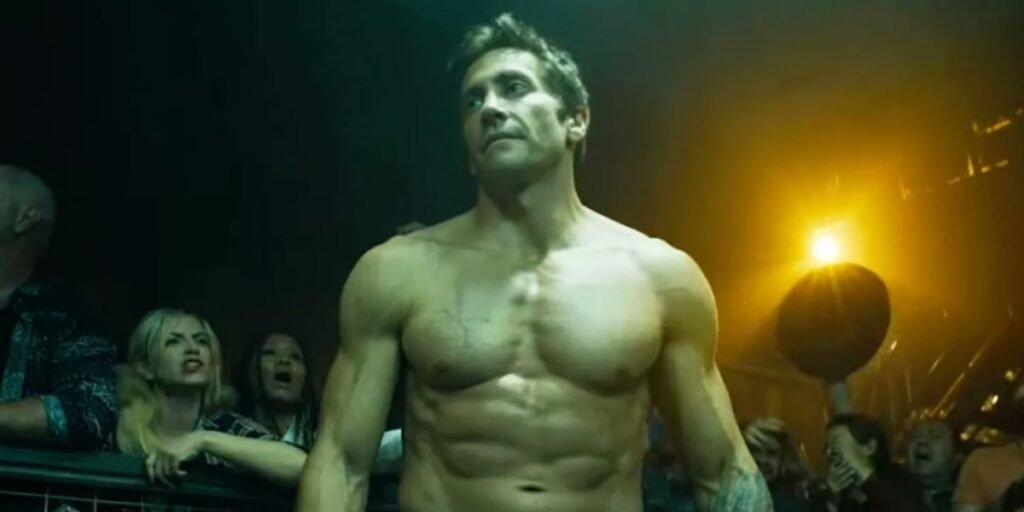 Jake Gyllenhaal stares down a potential opponent that is out of frame as he flexes his muscles in preparation for a fight in Road House. I Agents of Fandom