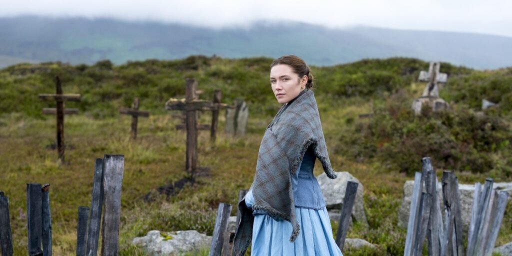 A brunette woman (Florence Pugh) stands on a grassy hilltop surrounded by cross-shaped headstones made of wood | Agents of Fandom