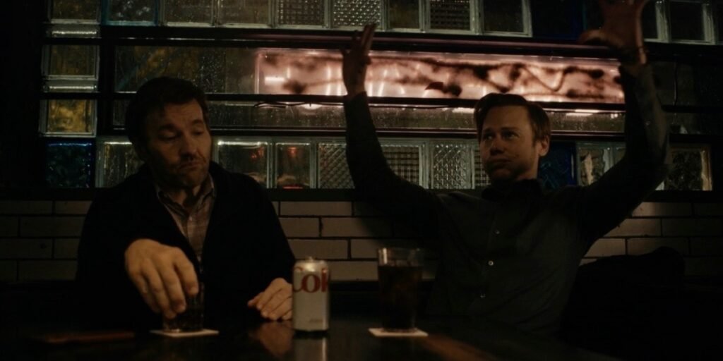 Joel Edgerton sipping a whiskey while Jimmi Simpson holds his hands in the air in Dark Matter Episode 1 | Agents of Fandom