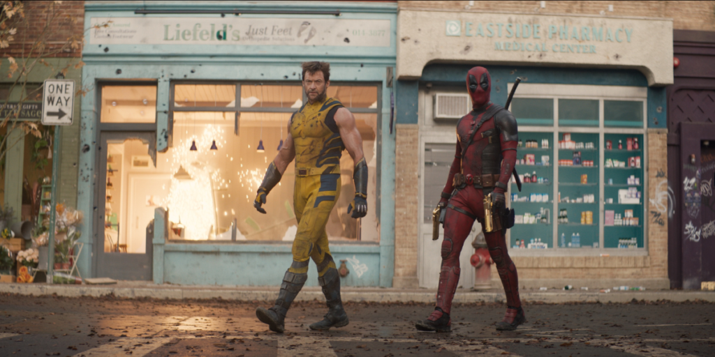 Action shot of Ryan Reynolds as Deadpool and Hugh Jackman as Wolverine in Deadpool & Wolverine walking through a city street in front of the store "Liefeld's Just Feet" | Agents of Fandom
