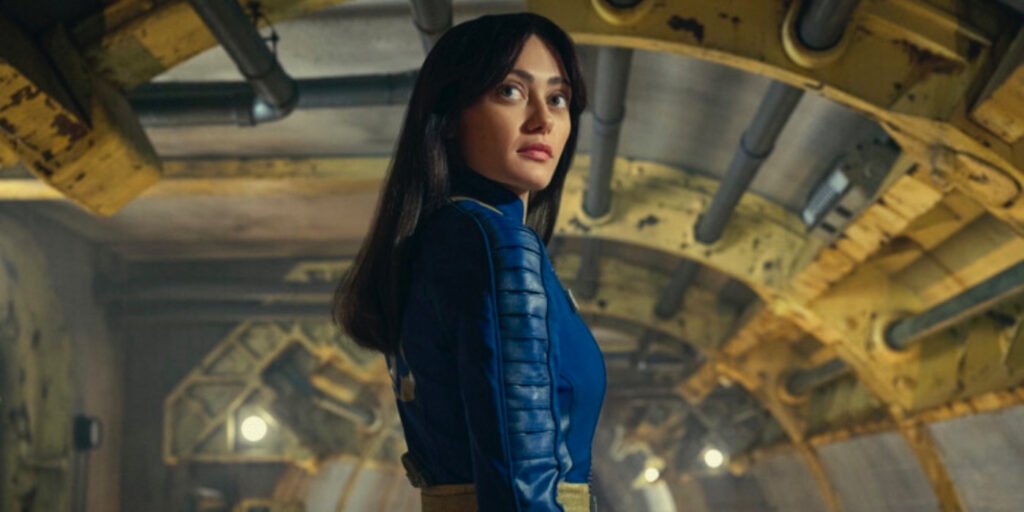 Ella Purnell as Lucy standing inside a vault looking over her shoulder in Fallout | Agents of Fandom