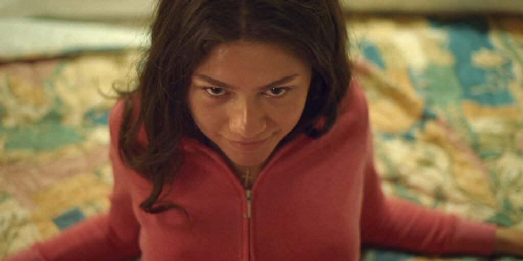 close-up of Zendaya leaning back on a bed wearing a pink hoodie in Challengers | Agents of Fandom