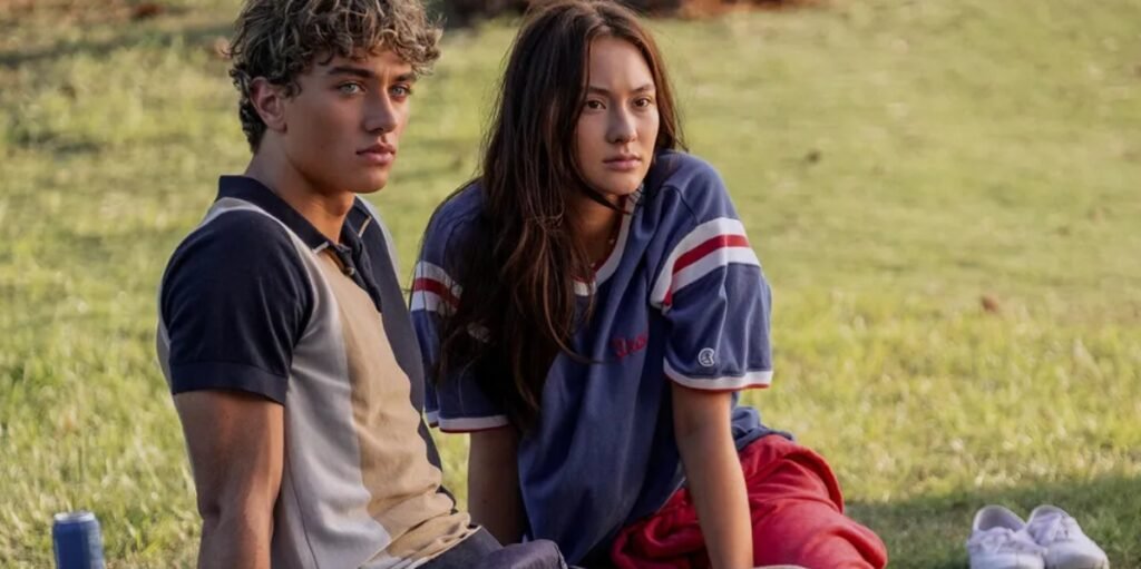 Isabel Conklin (Lola Tung) and Jeremiah Fisher (Gavin Casalegno) sit on the grass in Prime Video's The Summer I Turned Pretty | Agents of Fandom