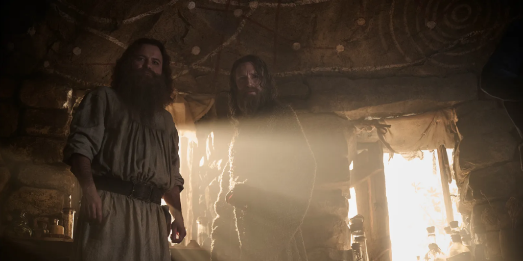 Tom Bombadil and The Stranger standing in Tom's house staring toward the camera with the sun beaming through the windows for Rings of Power Season 2 | Agents of Fandom