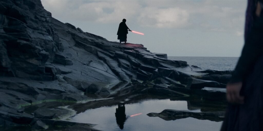 The Sith Lord holding out his lightsaber in his right hand on some rocks by an ocean in The Acolyte | Agents of Fandom