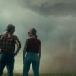 Glen Powell and Daisy Edgar Jones standing with a tonado in the distance in Twisters | Agents of Fandom