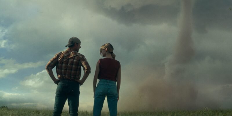 Glen Powell and Daisy Edgar Jones standing with a tonado in the distance in Twisters | Agents of Fandom