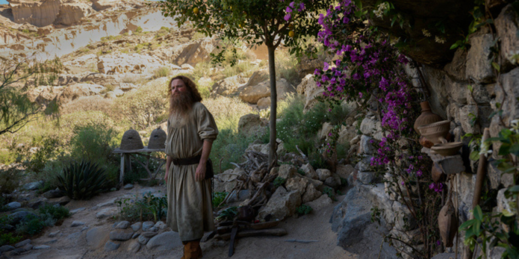 Ro Kinnear as the mysterious Tom Bombadil standing in front of his home in the fields of Rhǔn | Agents of Fandom