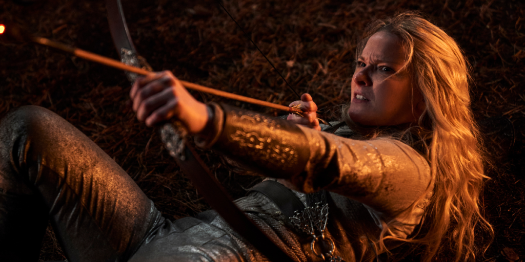 Morfydd Clark as Galadriel knocked to the ground with her bow drawn and ready to take fight | Agents of Fandom