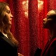 Emilia Pérez (Karla Sofía Gascón) and Rita (Zoe Saldaña) looking at one another in front of a red curtain in Emilia Pérez | Agents of Fandom