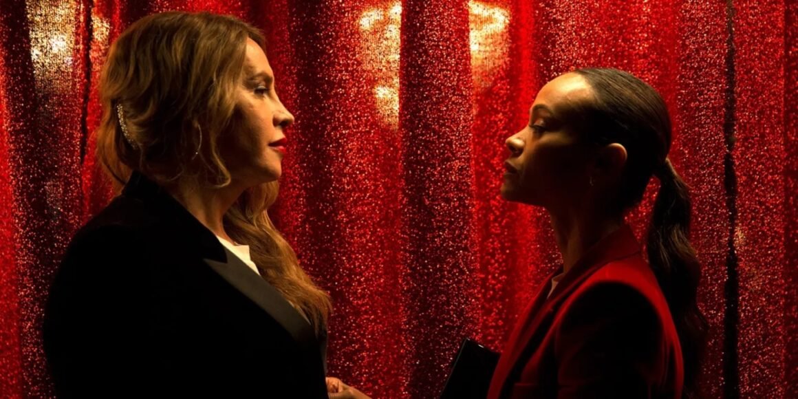 Emilia Pérez (Karla Sofía Gascón) and Rita (Zoe Saldaña) looking at one another in front of a red curtain in Emilia Pérez | Agents of Fandom