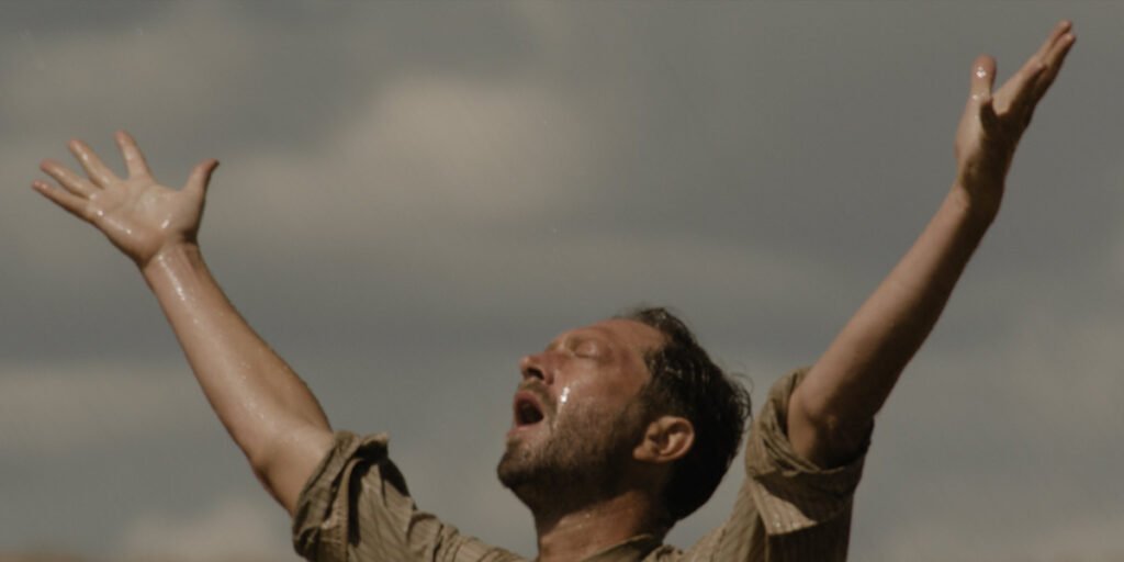 Wallace Grady (Ebon Moss-Bachrach) raising his hands in the air as he prays for rain to come in Hold Your Breath | Agents of Fandom