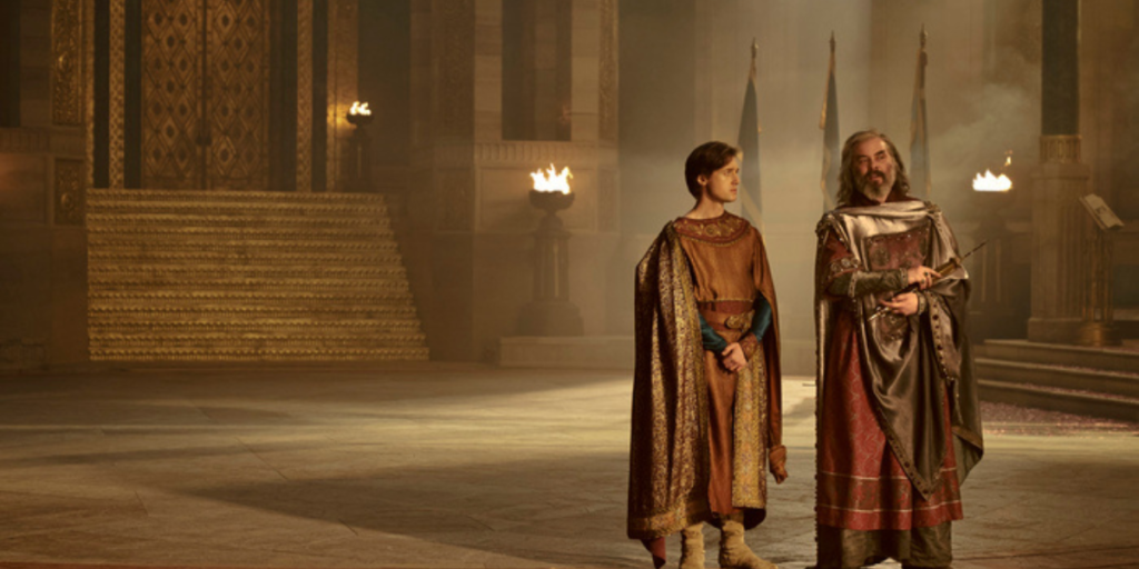 Trystan Gravelle as Pharazôn standing with Leon Wadham as his son Kemen in a giant hall in Númenor, looking over the island | Agents of Fandom