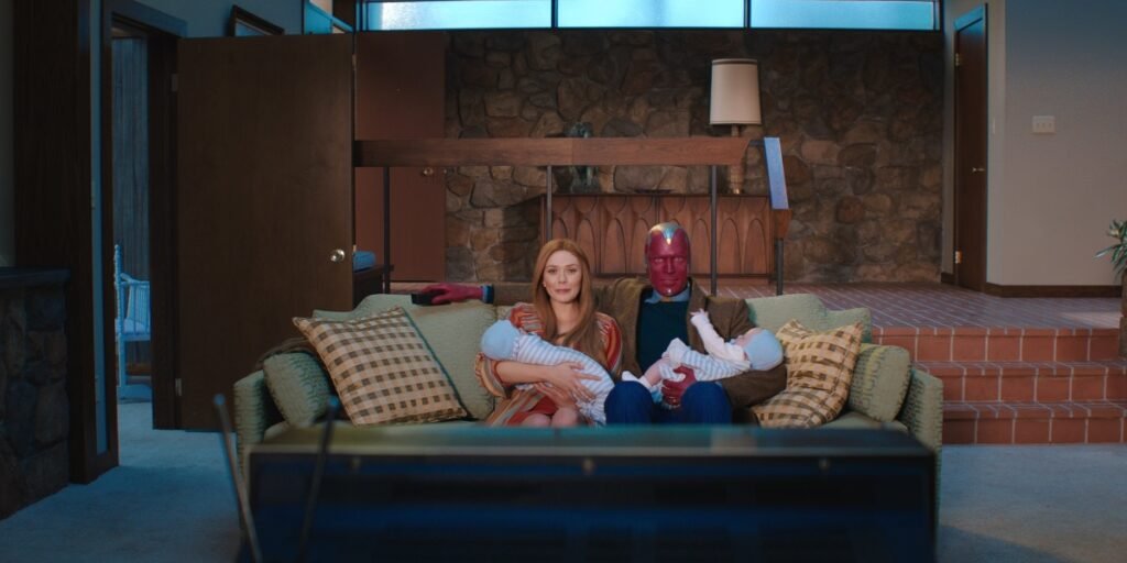 Elizabeth Olsen as Wanda and Paul Bettany as Vision sat on the couch in their living room holding their children in WandaVision | Agents of Fandom