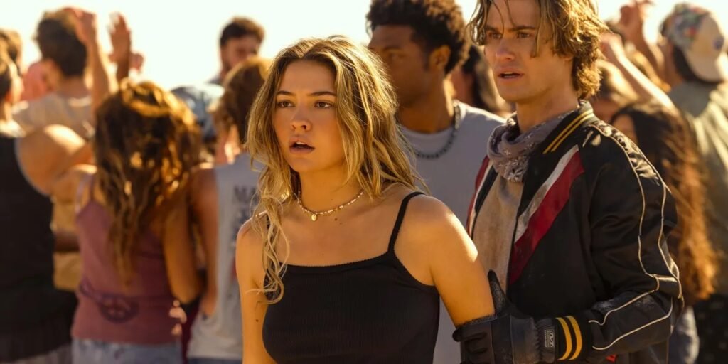 A man holding a woman's arm as people gather around them on the beach in Outer Banks | Agents of Fandom