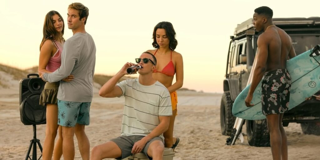 A group of teenagers hang out on the beach. The boy in the center sits on the cooler and drinks a beer. | Agents of Fandom