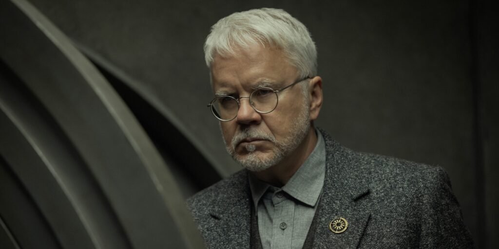 Tim Robbins closely examining something in Silo Season 2 | Agents of Fandom