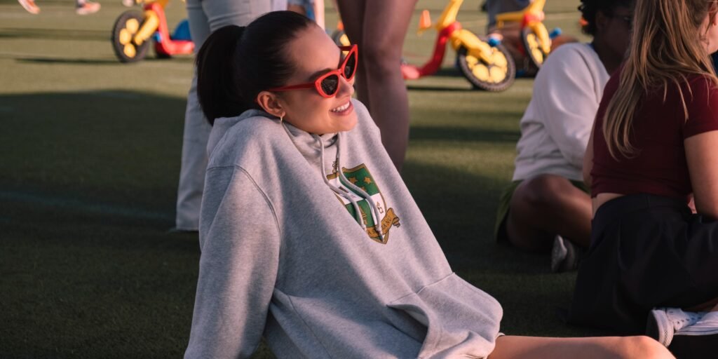 Belly (Lola Tung) wears red sunglasses and an oversized grey sweatshirt laying on the grass. | Agents of Fandom 