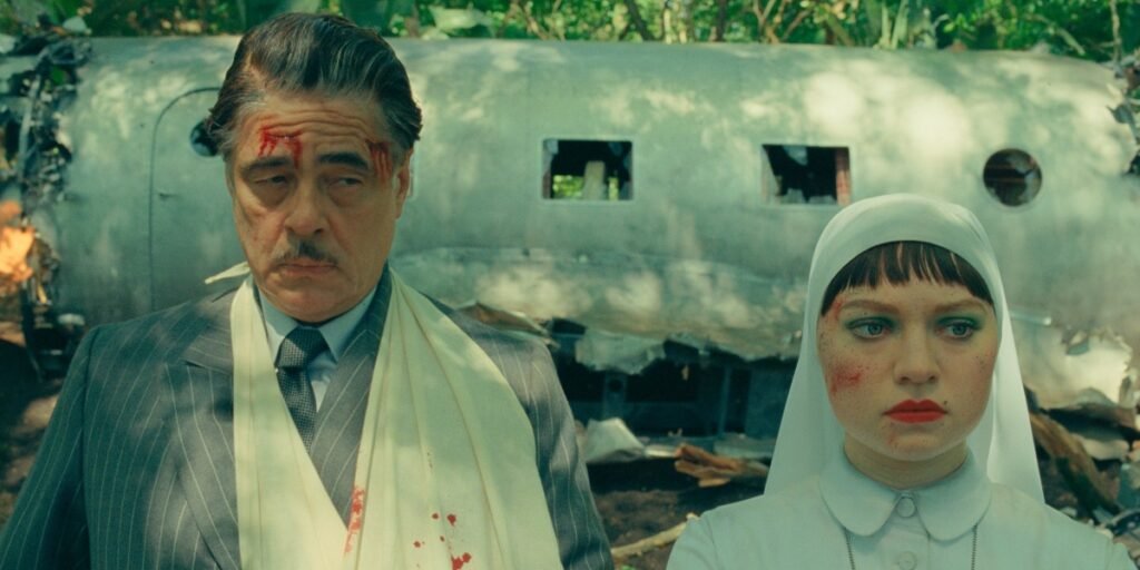 Benicio Del Toro and Mia Threapleton outside a plane crash in the forest in The Phoenician Scheme | Agents of Fandom