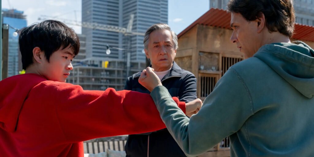 Daniel LaRusso (Ralph Macchio) blocking a punch from Li Fong (Ben Wang) while Mr. Han (Jackie Chan) watches in Karate Kid: Legends | Agents of Fandom