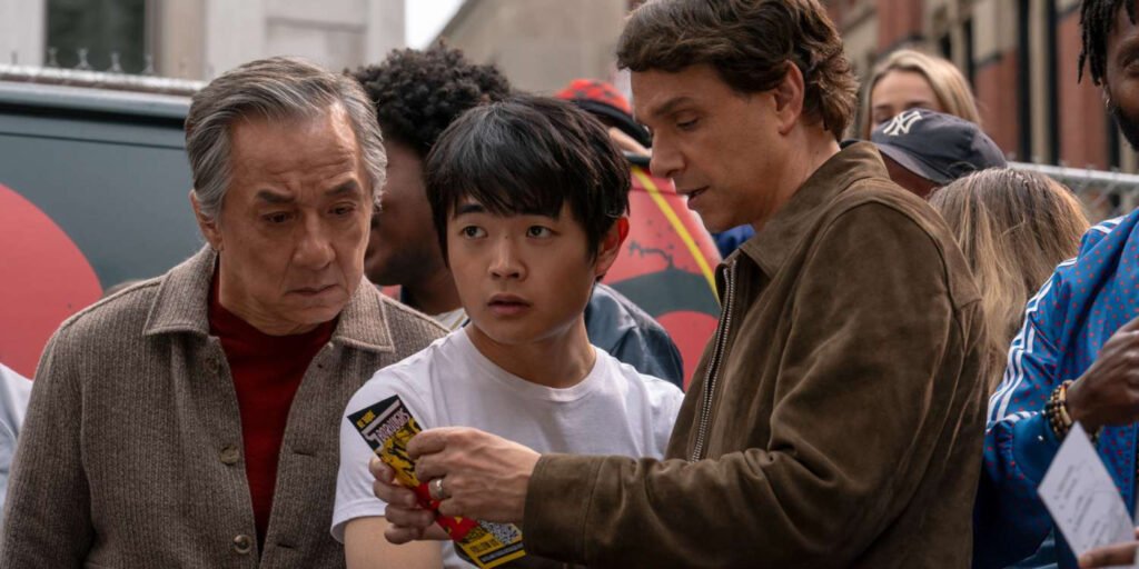 Mr. Han (Jackie Chan) and Daniel LaRusso (Ralph Macchio) looking at a pamphlet while Li Fong (Ben Wang) watches a fight in Karate Kid: Legends | Agents of Fandom