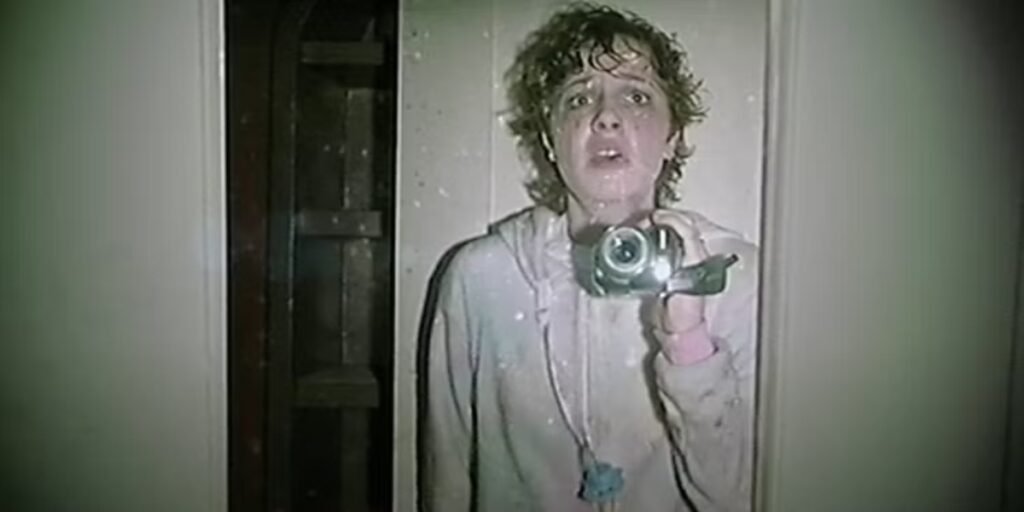 A woman holds up a video camera to a mirror in V/H/S/Halloween